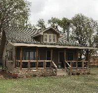A small house with a porch in the middle of a field.