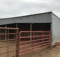A horse stable with a red gate in front of it.