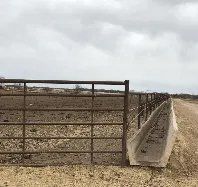 A fence with a trough in the middle of a dirt field.