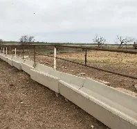 A concrete trough is sitting in the middle of a dirt field next to a fence.