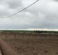 A dirt field with a fence in the foreground and a cloudy sky in the background.