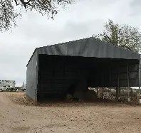 A large shed is sitting in the middle of a dirt field.