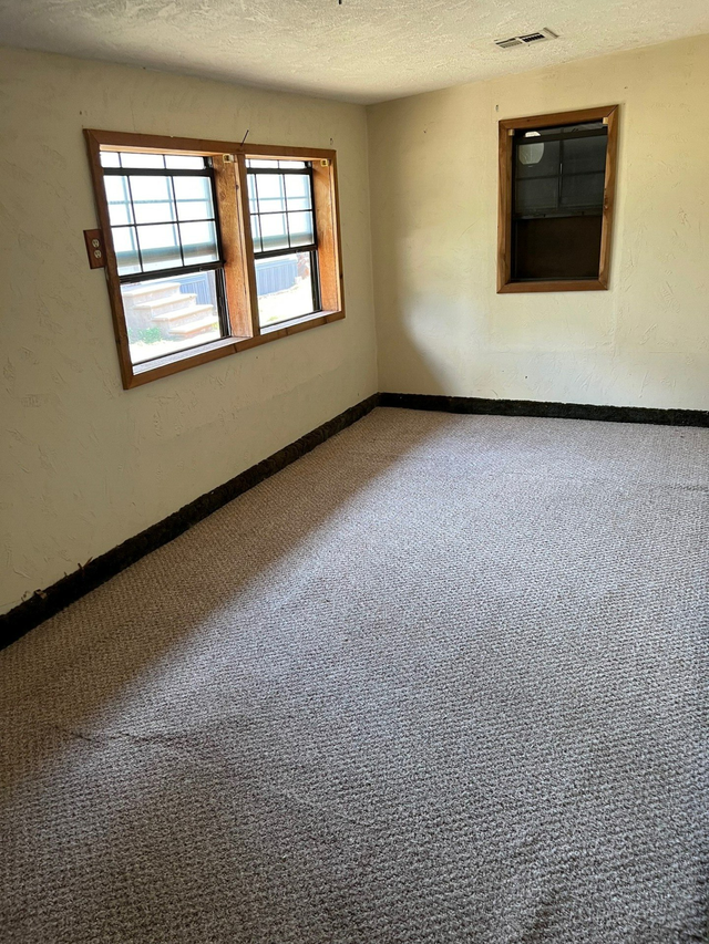 An empty room with a carpeted floor and two windows.