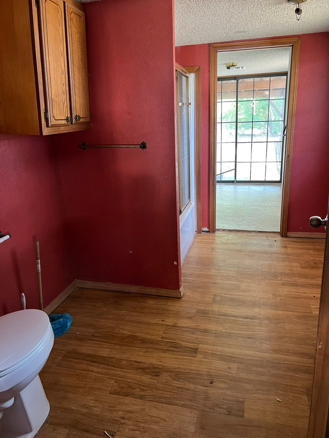 A bathroom with a toilet , cabinets , and hardwood floors.