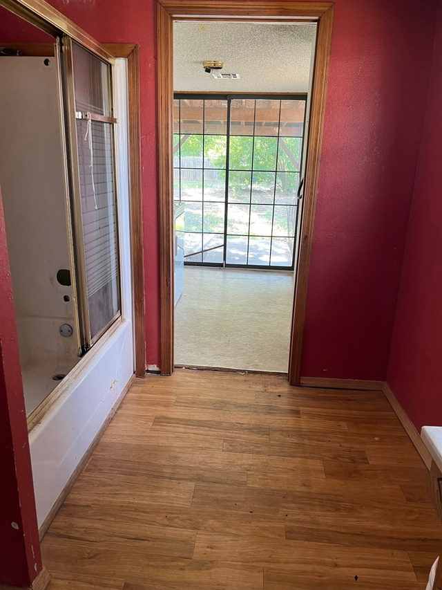 A hallway with wooden floors and red walls leading to a bathroom.