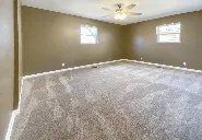 An empty room with a ceiling fan and a lot of carpet.