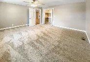 An empty living room with a carpeted floor and a ceiling fan.