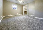 An empty room with a gray carpet and a ceiling fan.