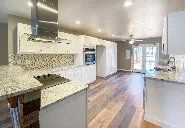 A kitchen with white cabinets , granite counter tops , stainless steel appliances and hardwood floors.