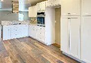 A kitchen with white cabinets and wooden floors.