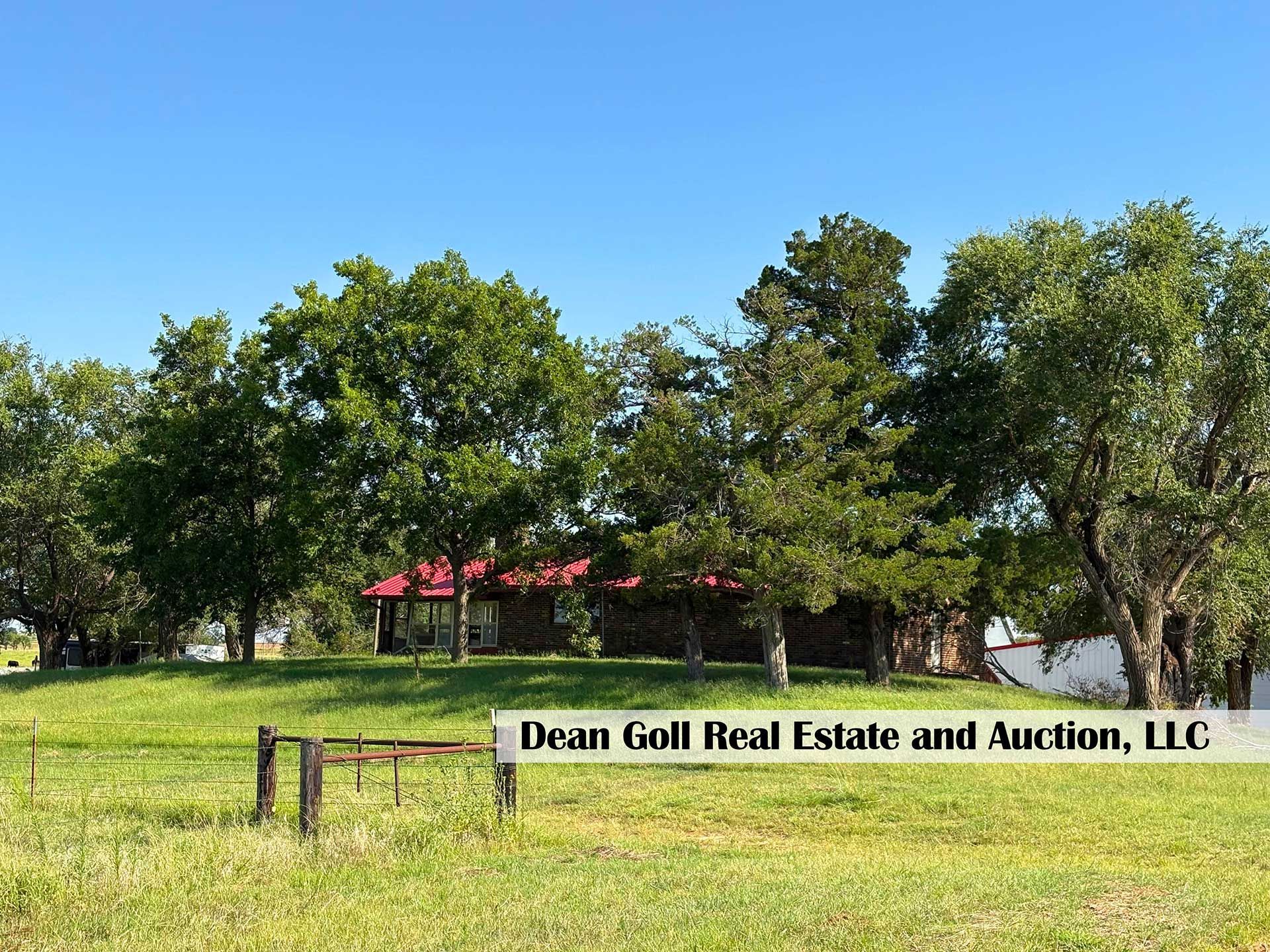 ranch-style home with a red roof, surrounded by trees on a green grassy hill