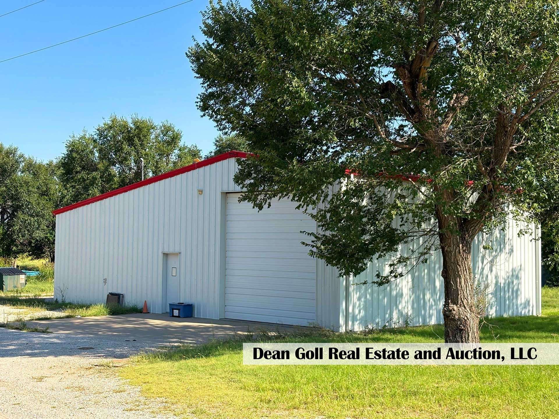 white metal warehouse with red trim and a large tree on a sunny day