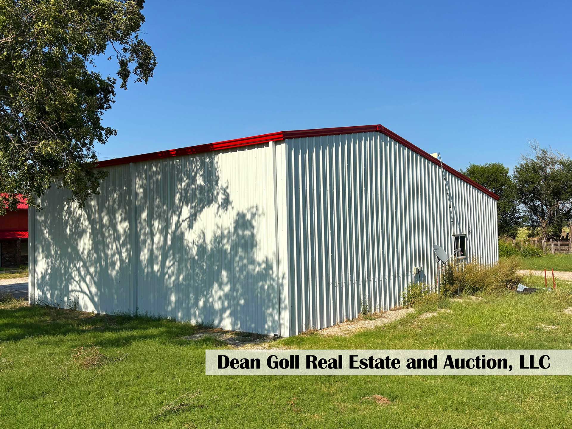a metal barn with a red roof and white siding on a grassy field under a blue sky