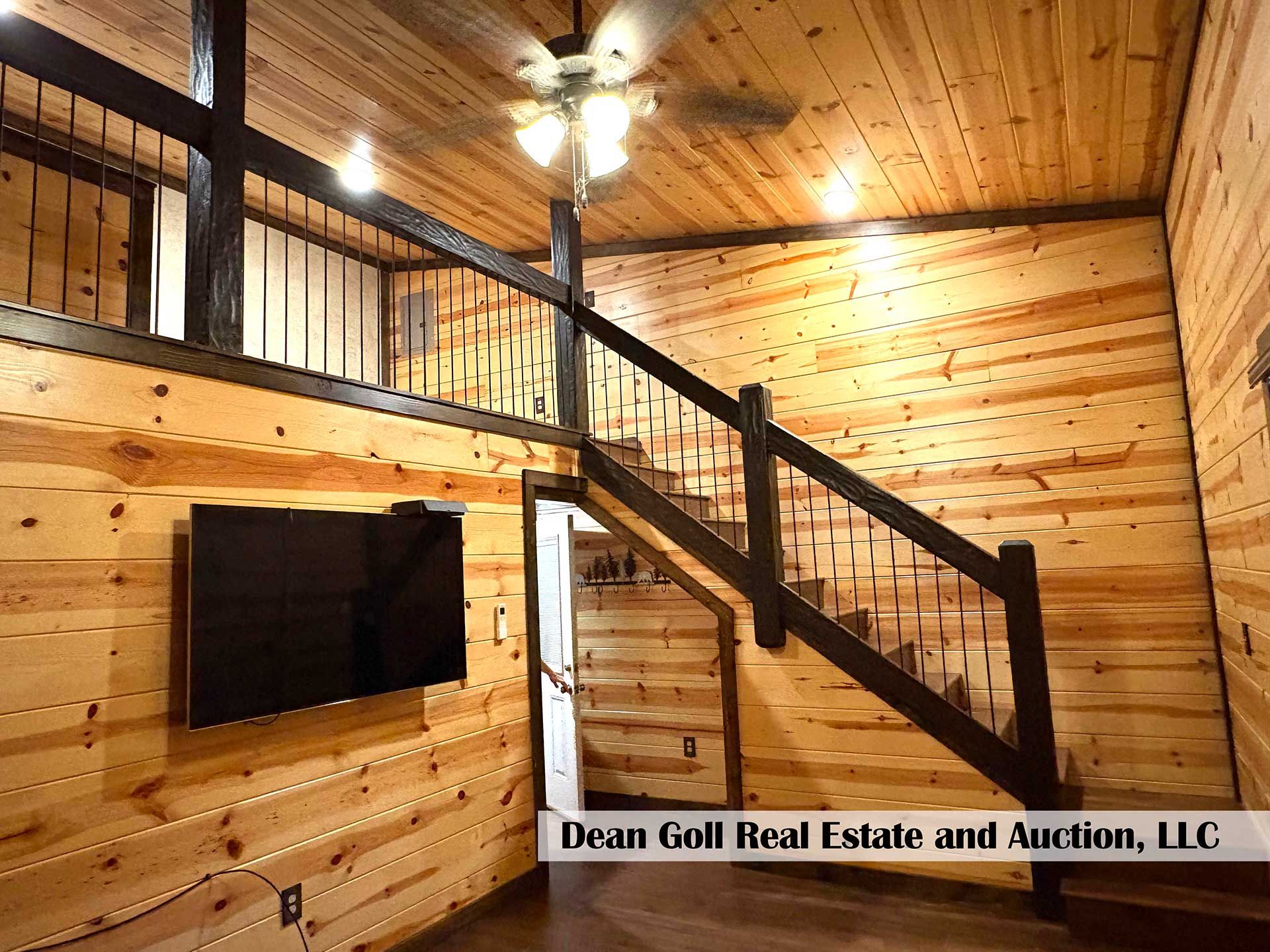 interior of a cabin with wooden walls, a dark staircase, and a mounted TV