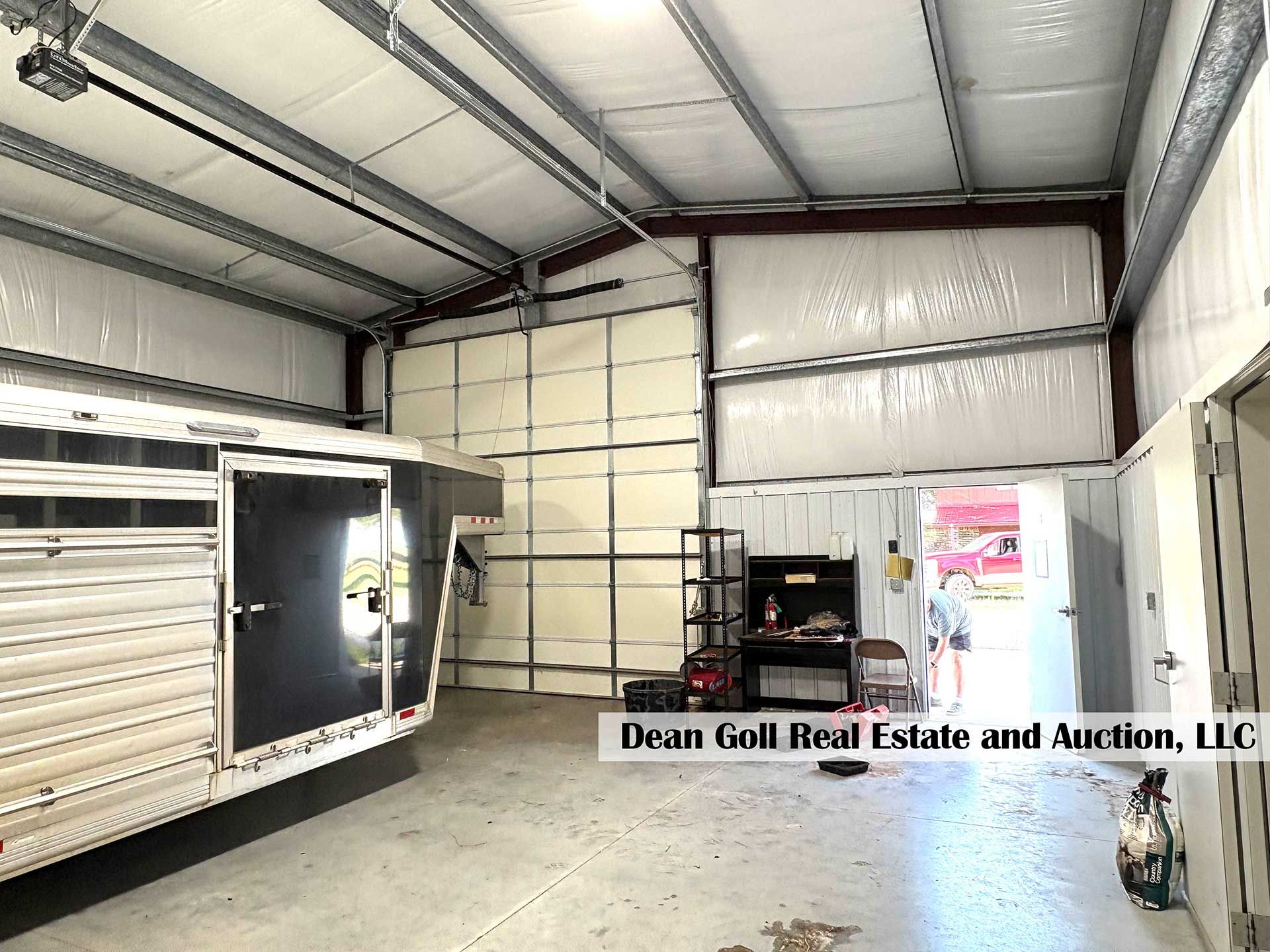 inside of a garage with a horse trailer, workbench, open door, and white walls