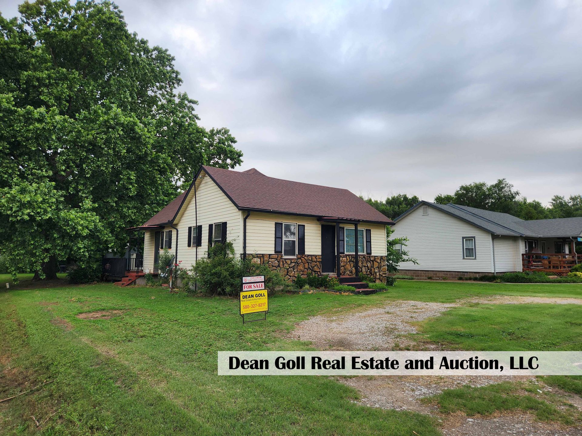 A small, beige house for sale, with a brown roof and stone facade, situated on a grassy lot. A 