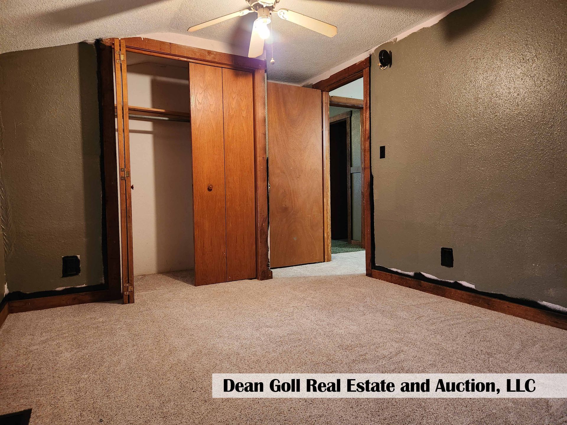 A bedroom with a closet, tan carpet, and olive green walls. There is a doorway leading to another room.