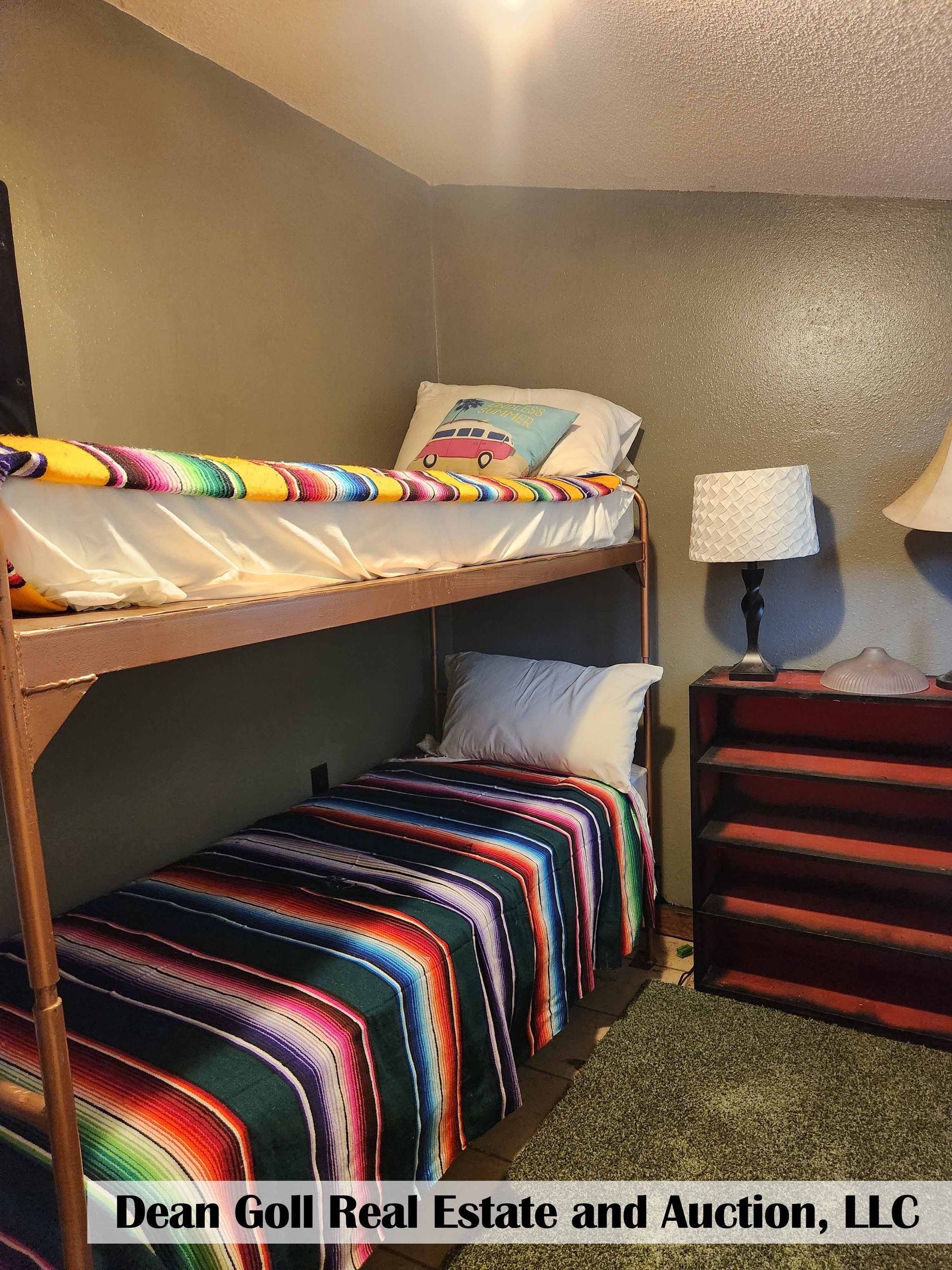Bunk beds in a small room, featuring colorful blankets, pillows, and a nightstand with lamps.