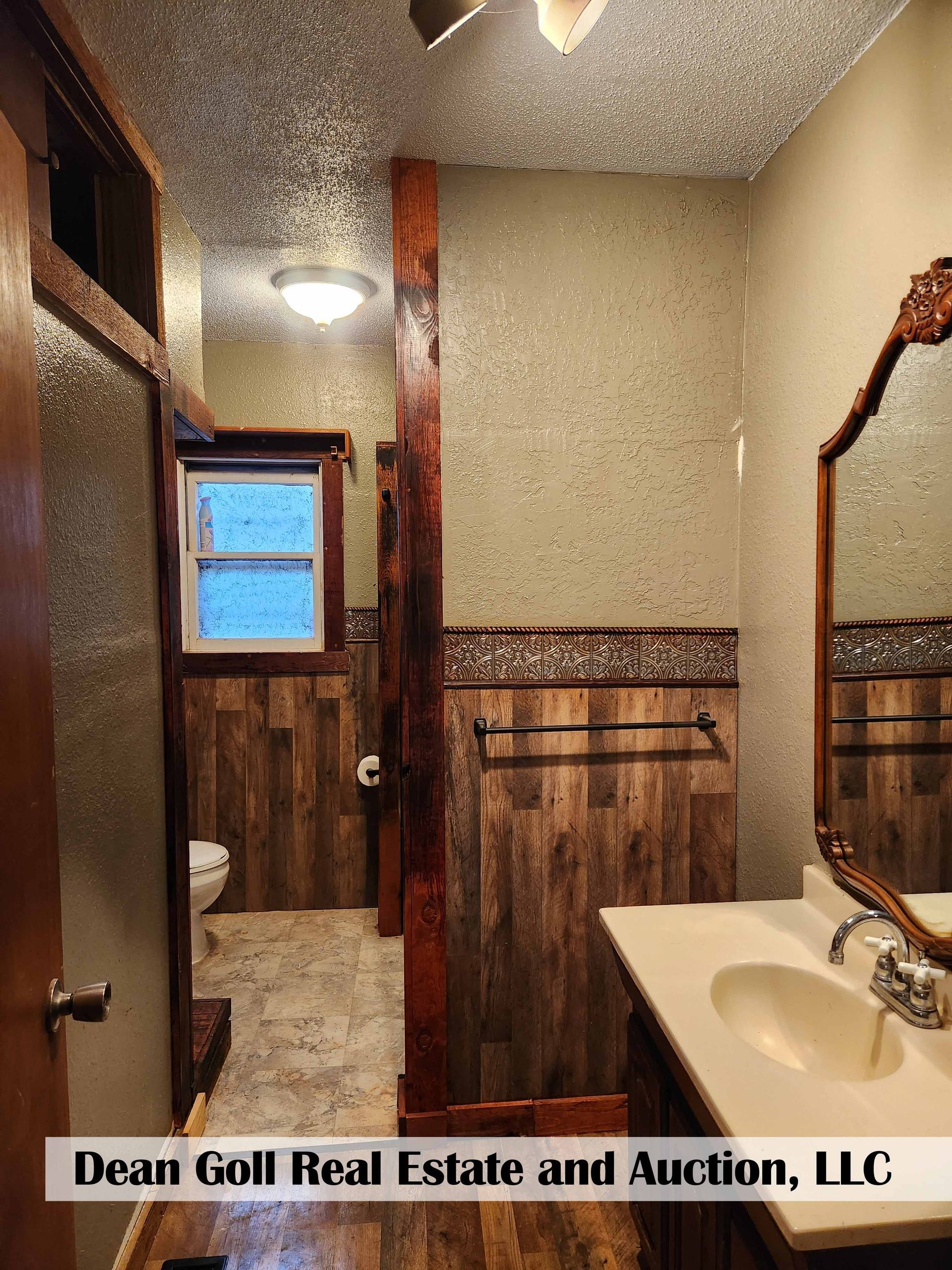 Rustic-style bathroom with wood paneling, a vanity with a double sink, and a toilet in a separate room.