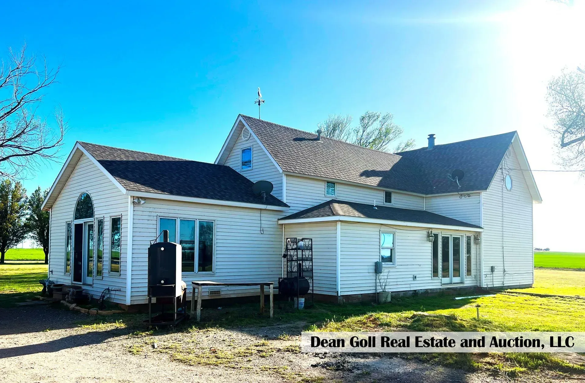 White farmhouse with multiple additions on a sunny day. A metal container sits next to the house, with green grass and a field in the background.
