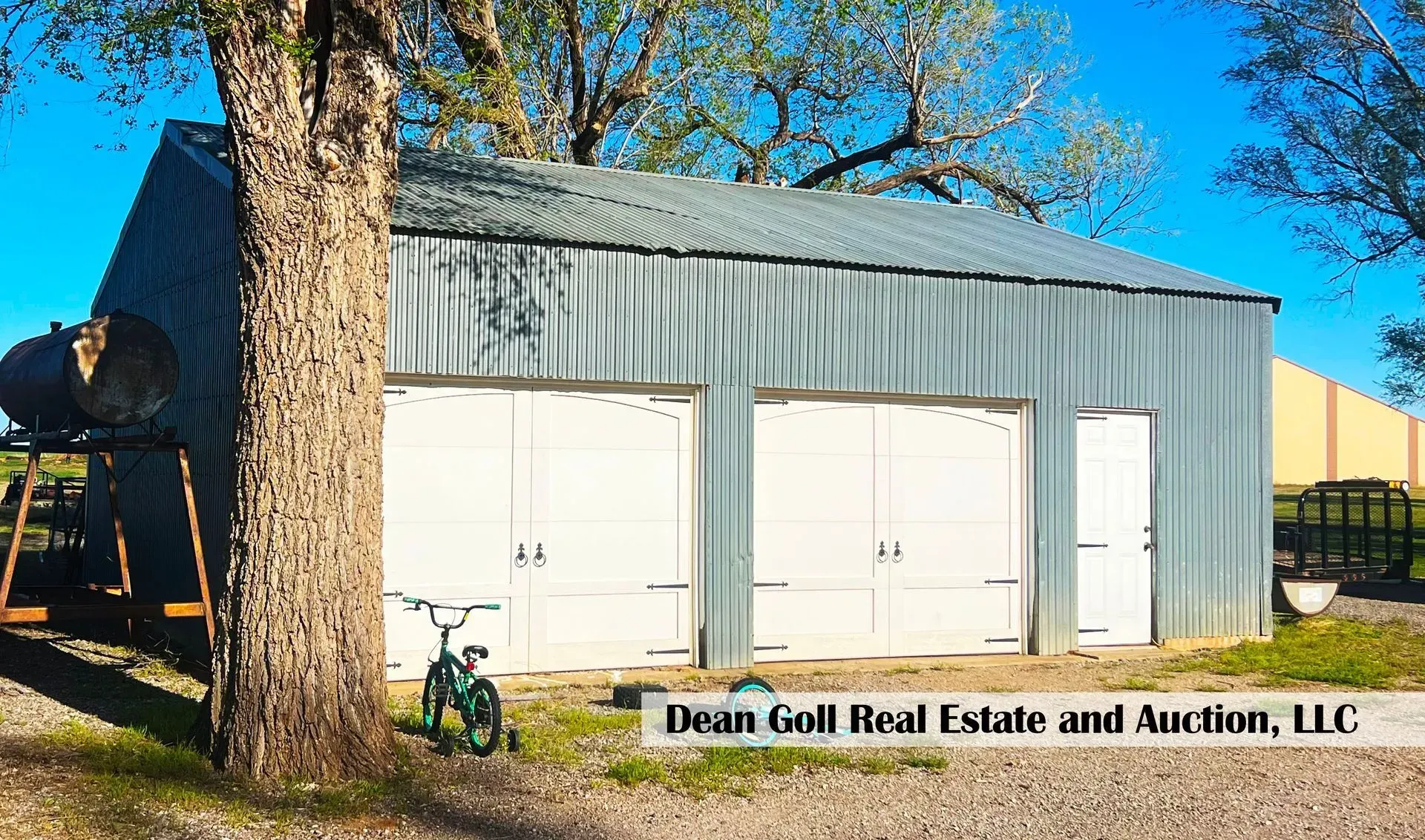 Metal garage with two large doors and a single door. A tree and bicycle are in the foreground.