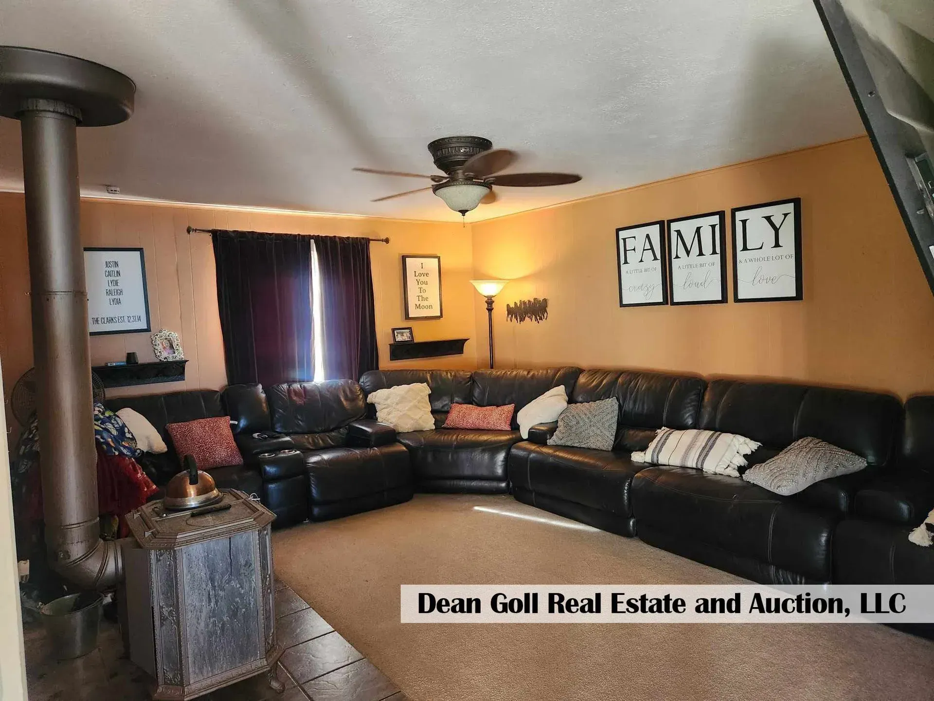 A living room with a large black sectional sofa, a brown carpet, and a wood-burning stove. 
