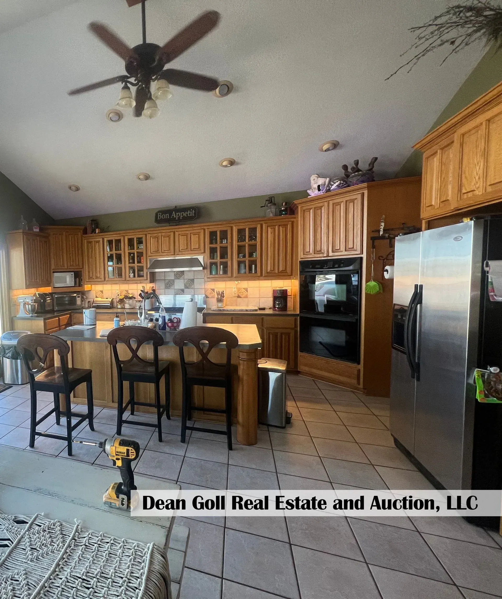 Kitchen with wood cabinets, island with bar stools, stainless steel refrigerator, and a ceiling fan.