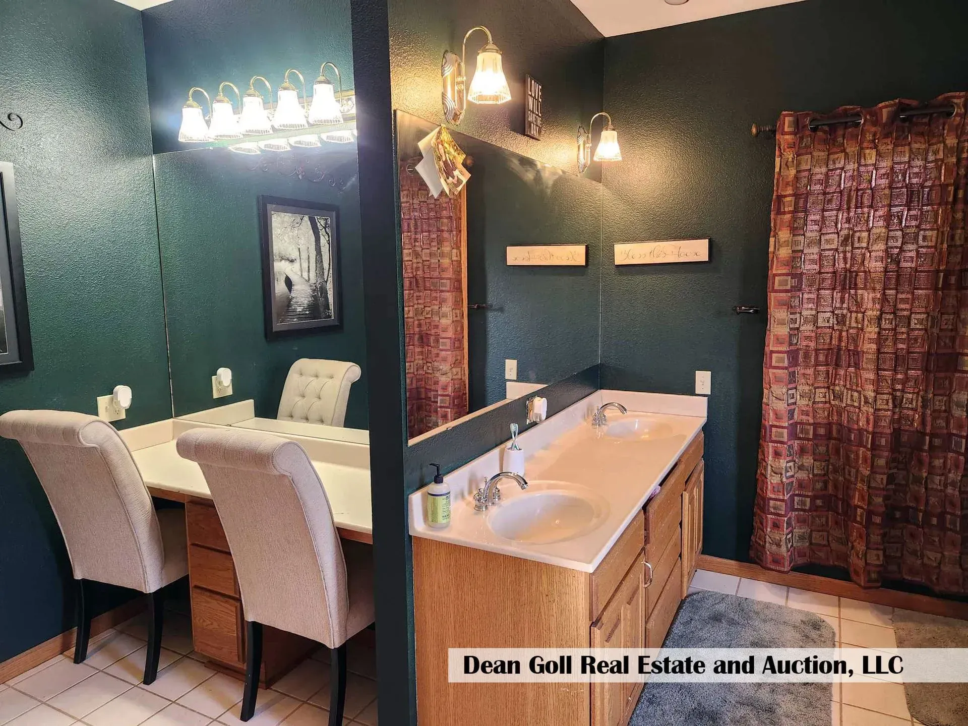 A bathroom with two sinks, a vanity, and a dark green wall. Two matching chairs sit in front of the vanity.