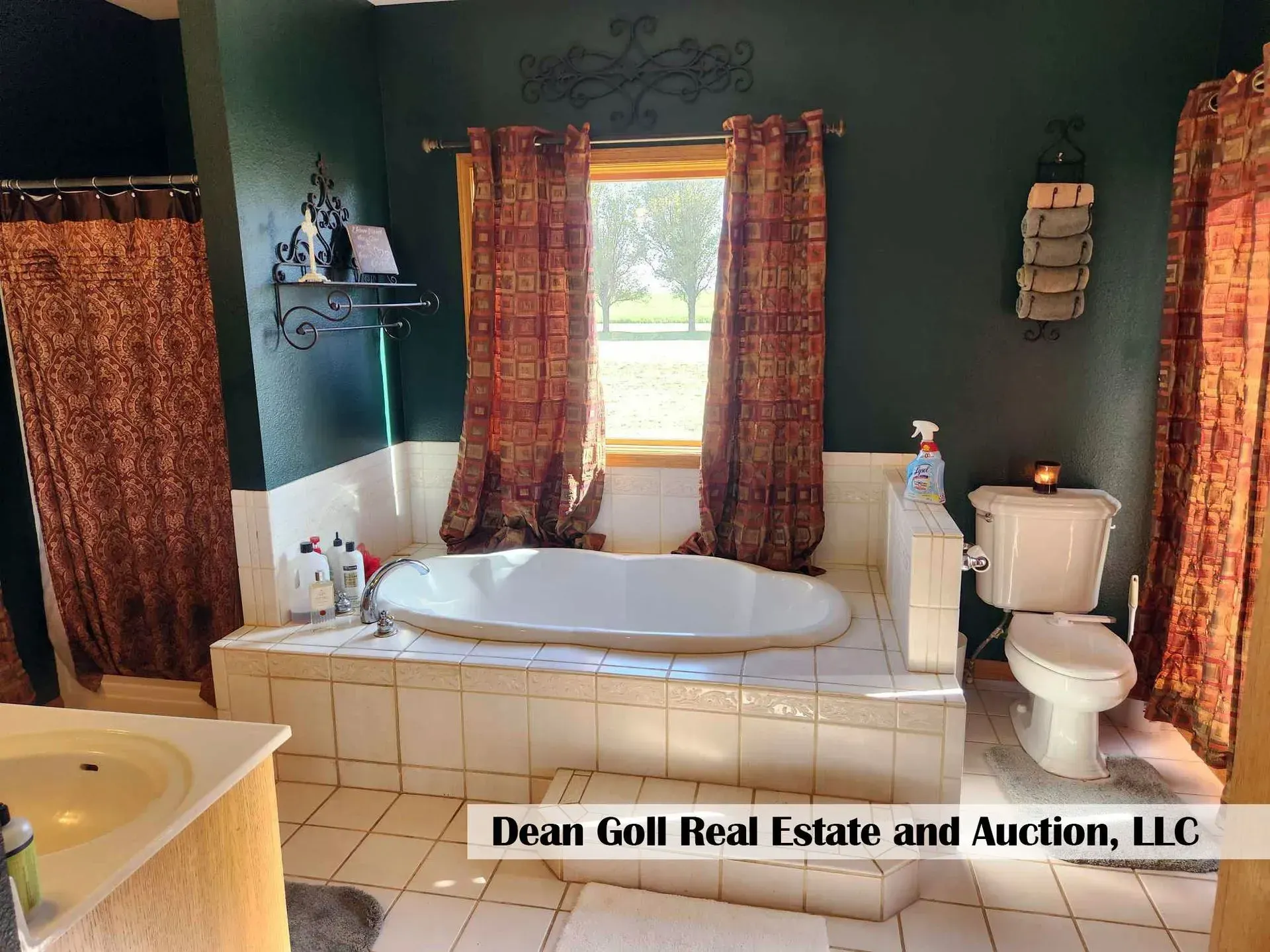 Bathroom with a large oval tub, toilet, and window. Dark green walls, beige tile, and red patterned curtains.