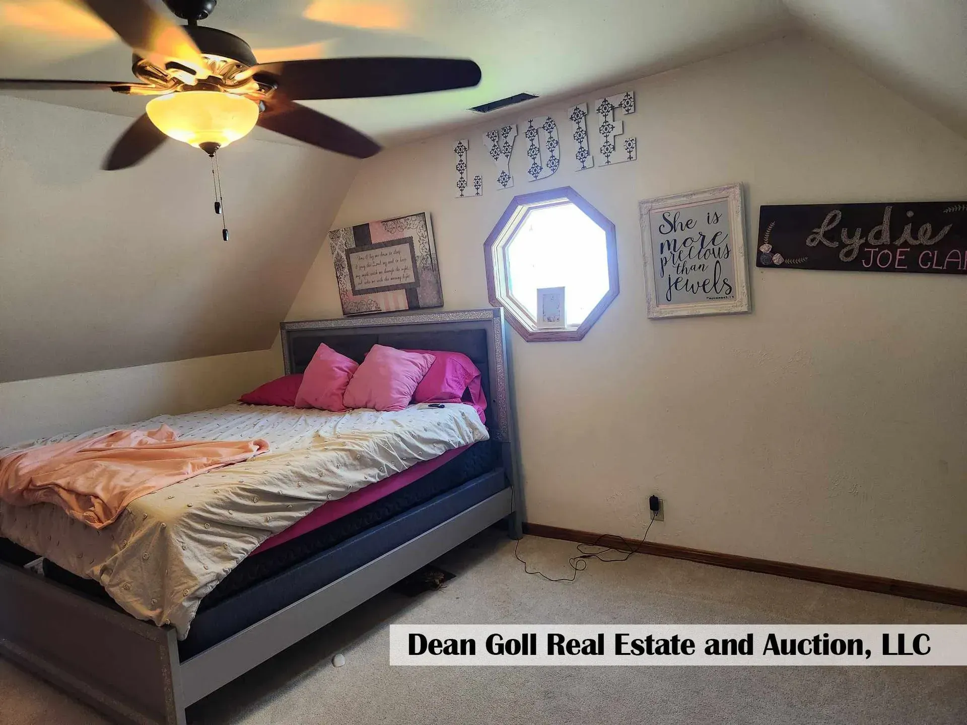 Bedroom with bed, pink pillows, and a ceiling fan. There's a round window and decorations on the wall.