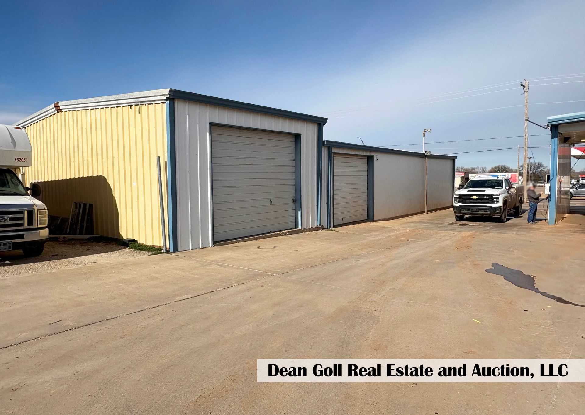 Metal storage buildings with roll-up doors, on a gravel lot under a blue sky, a truck parked nearby.