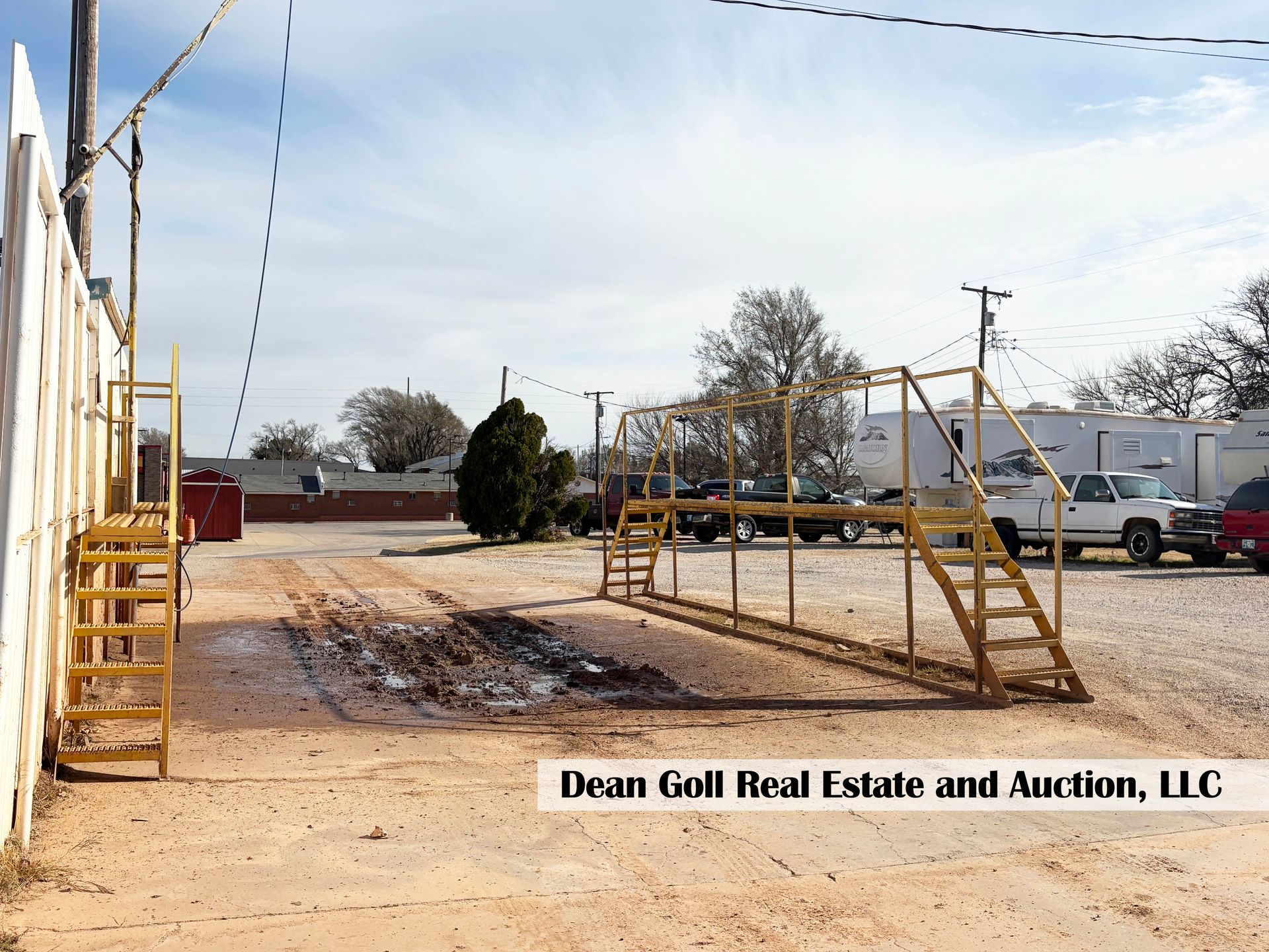 Yellow metal structures, possibly ramps, on a dirt lot; utility poles and parked vehicles in the background.