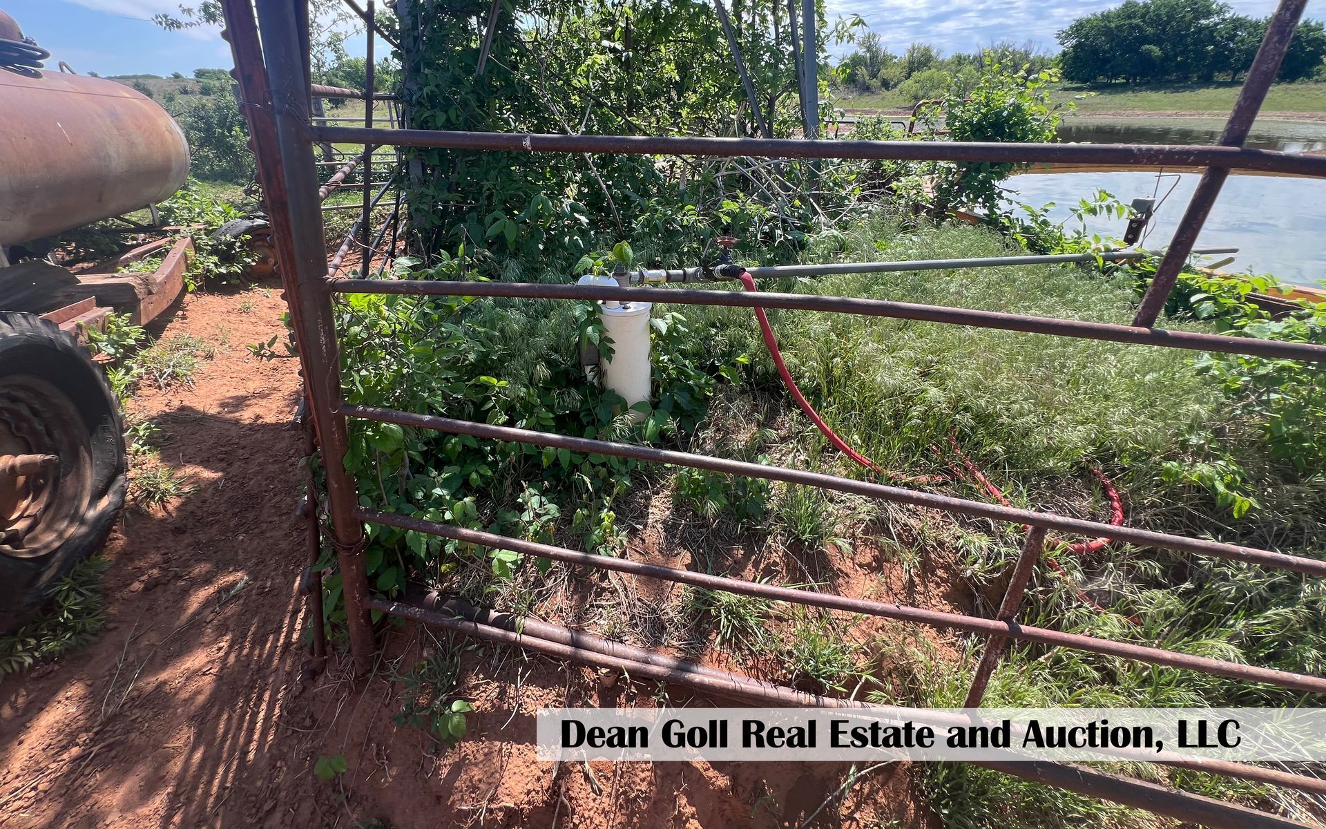 A fence with a hose attached to it in a field next to a body of water