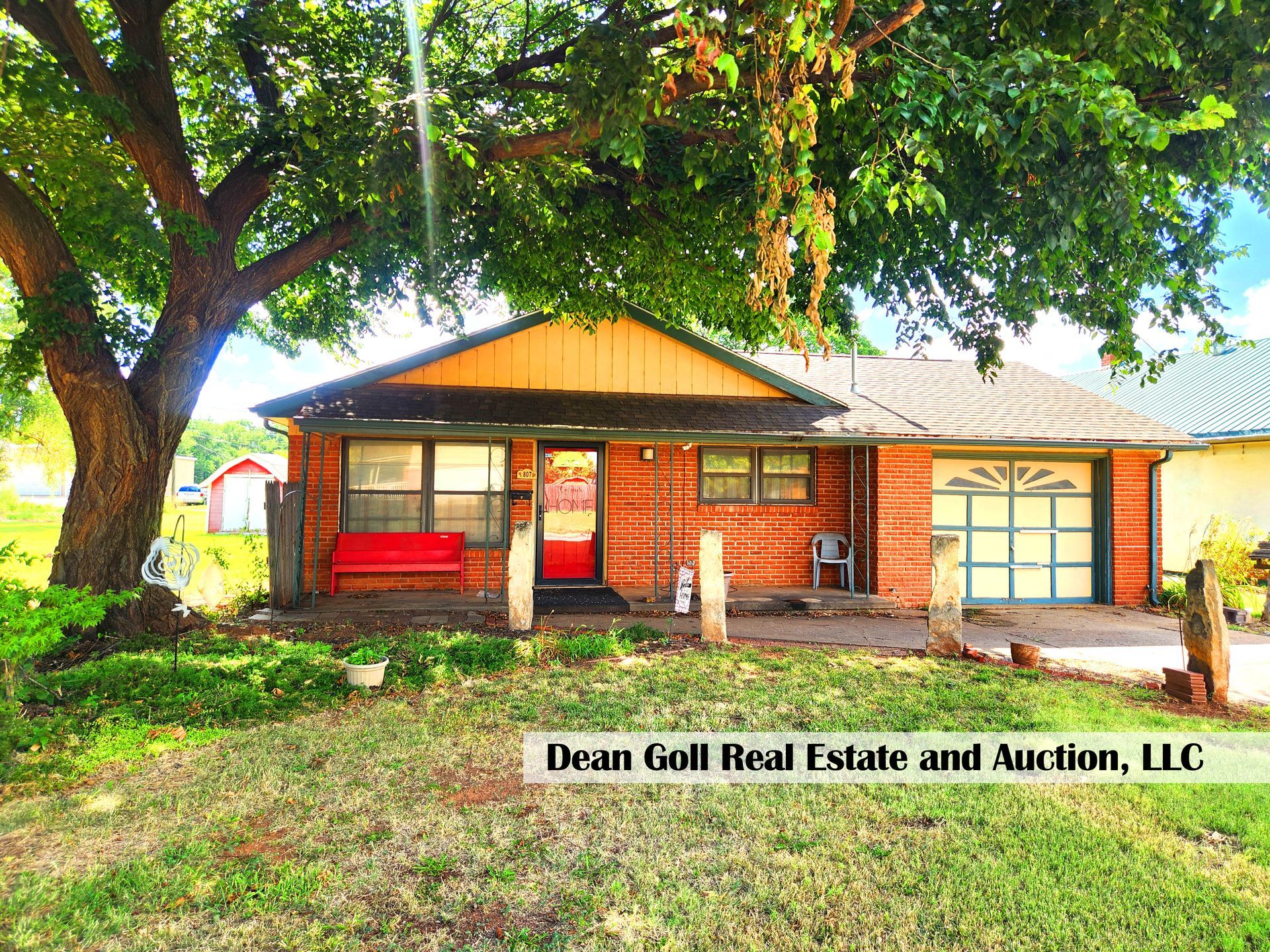 Brick ranch home with a red door and garage, a large tree shades the front yard.