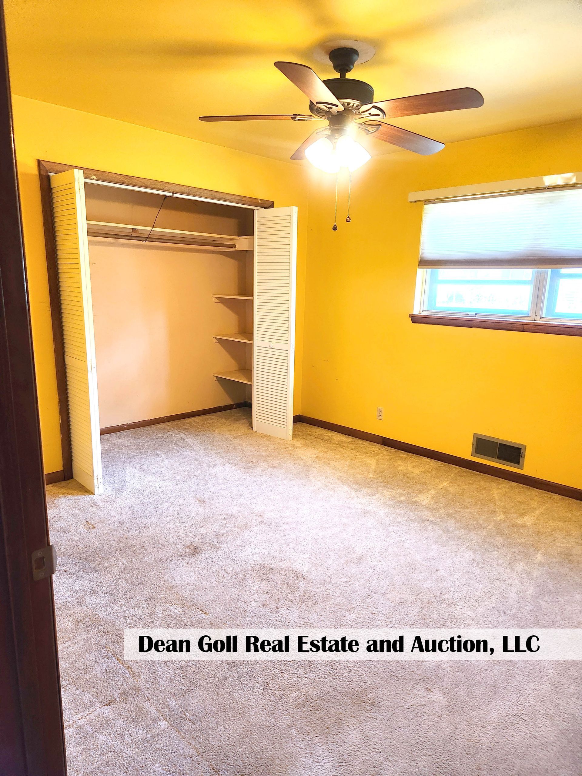 Empty bedroom with yellow walls, beige carpet, and a closet. A ceiling fan hangs from the ceiling.