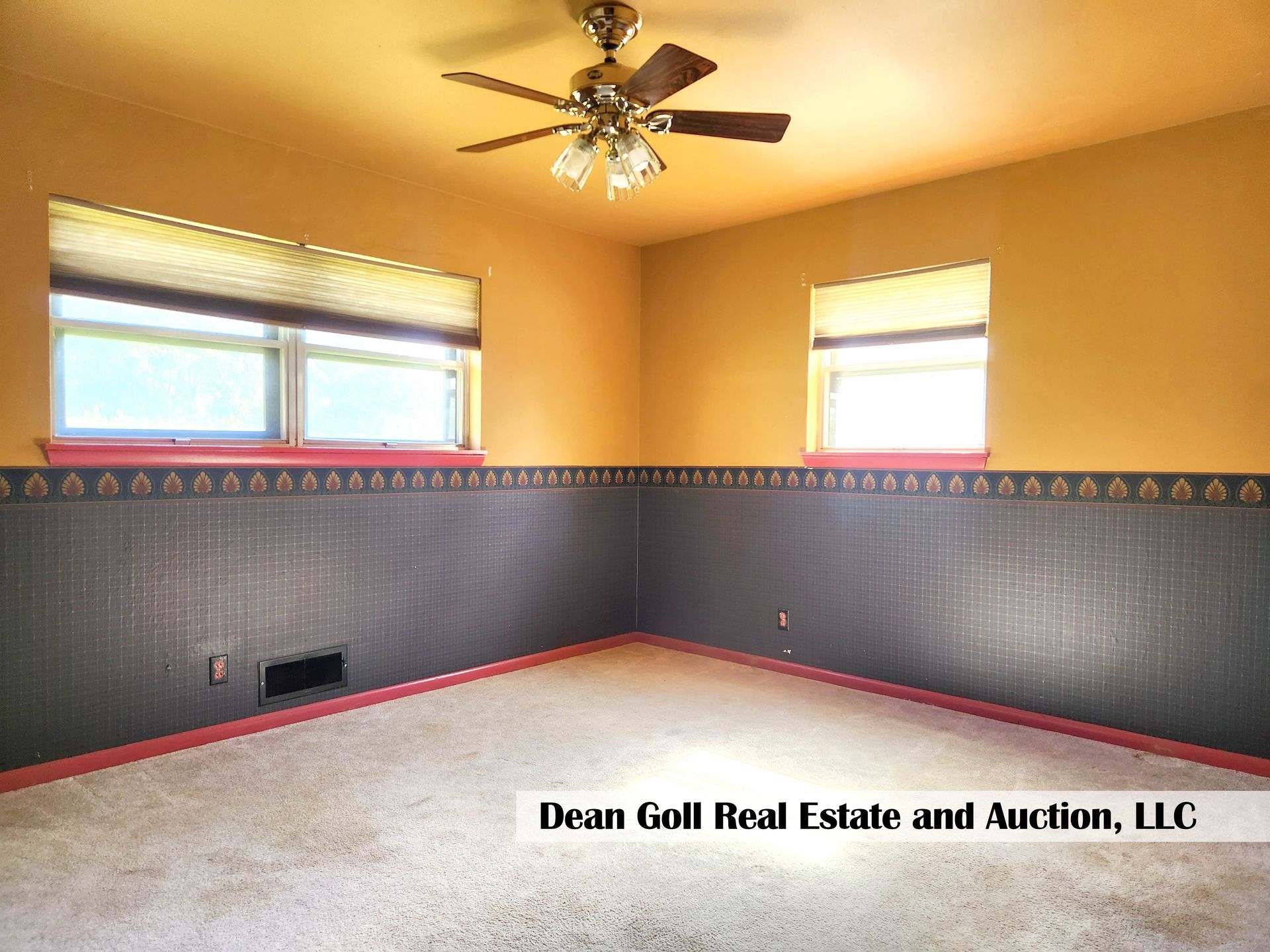 Empty room with gold walls, a dark patterned wainscoting, two windows with blinds, and a ceiling fan.