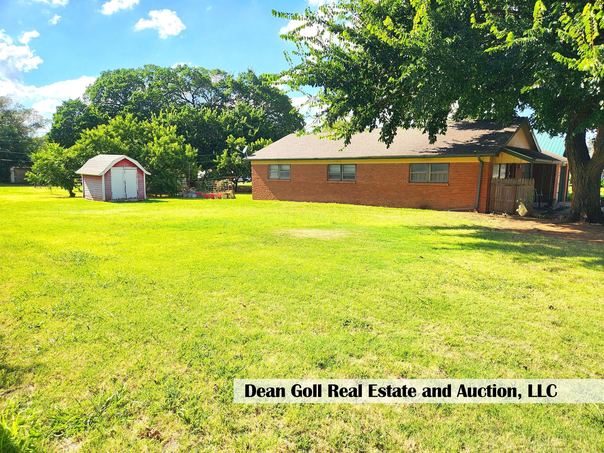 A brick house with a green lawn and a small shed under a blue sky.