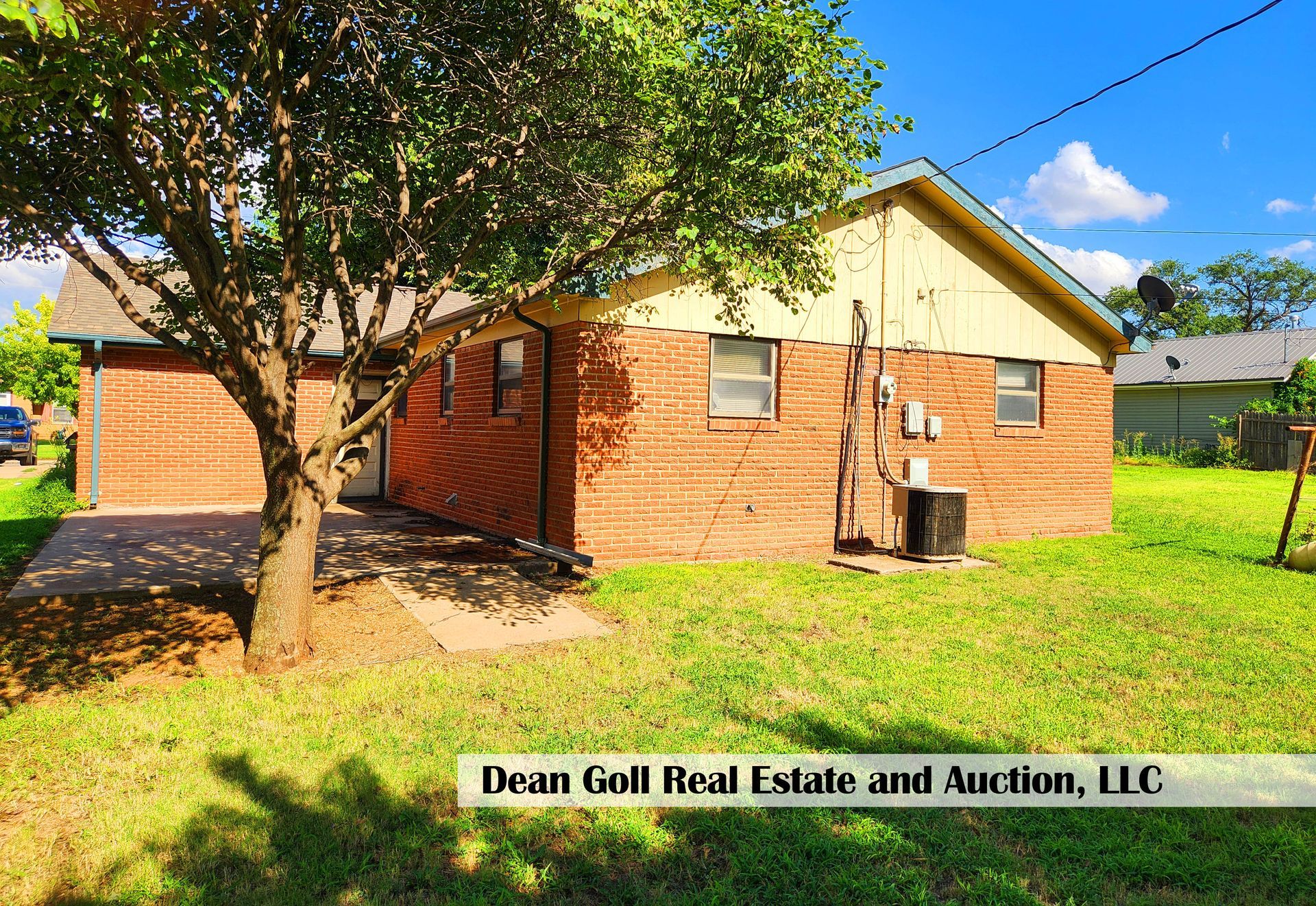 Side view of a red brick house with a tree in the foreground, and green grass.