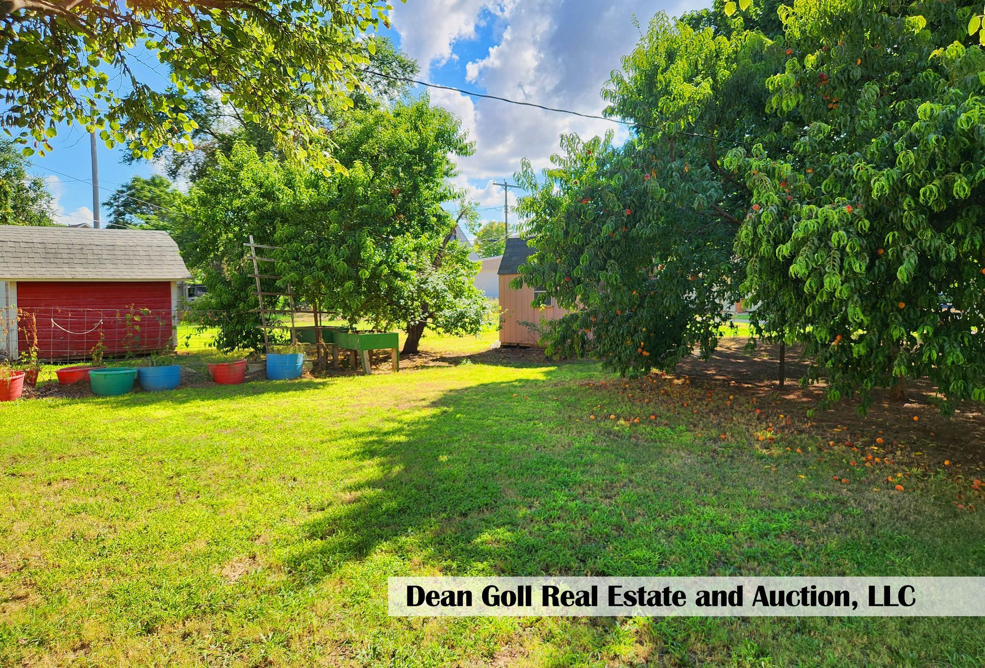 Lush green backyard with a red shed, trees, and colorful pots, under a partly cloudy sky.