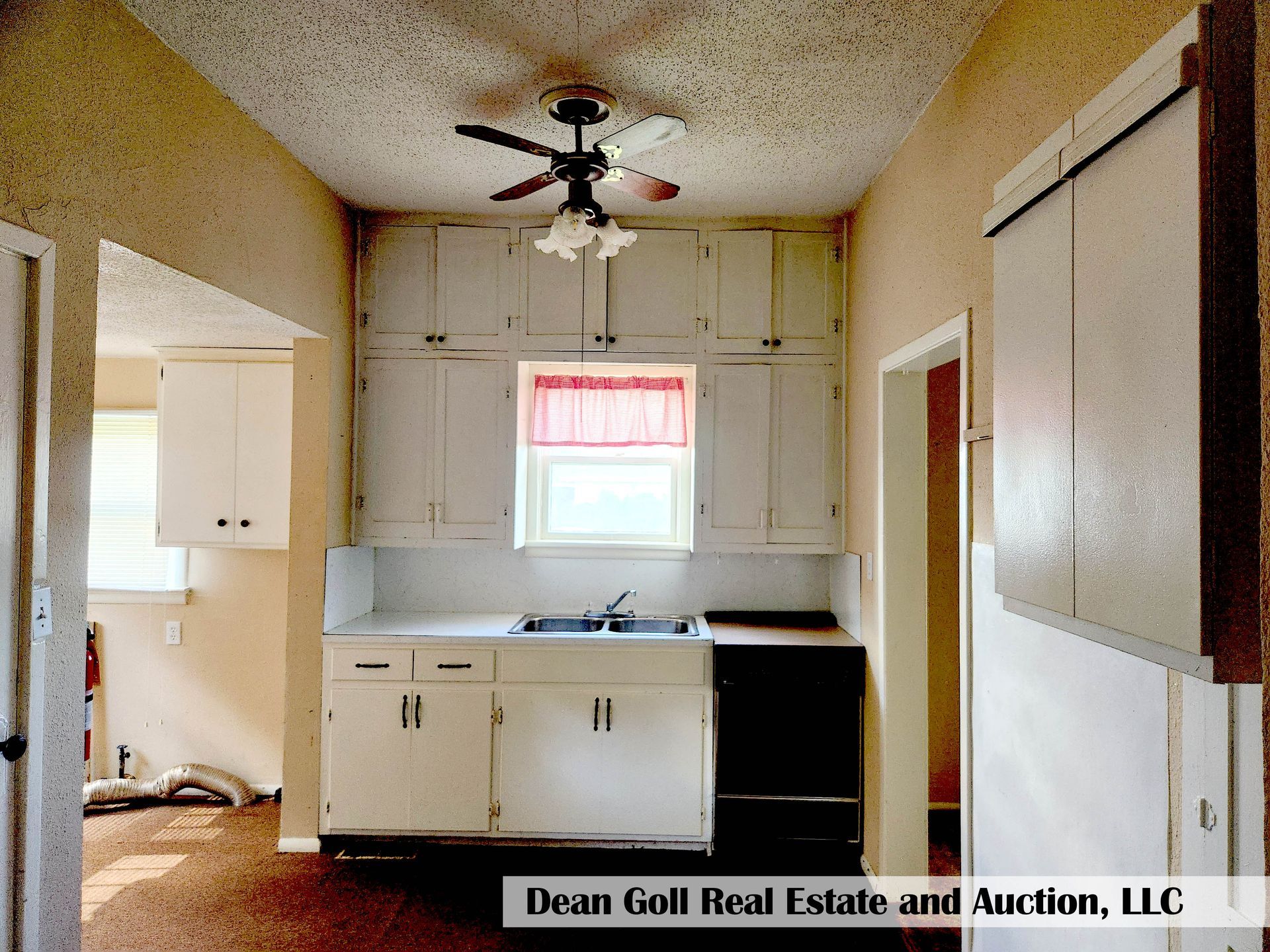 A small, outdated kitchen with white cabinets, a window, and a black stove. The walls are beige.