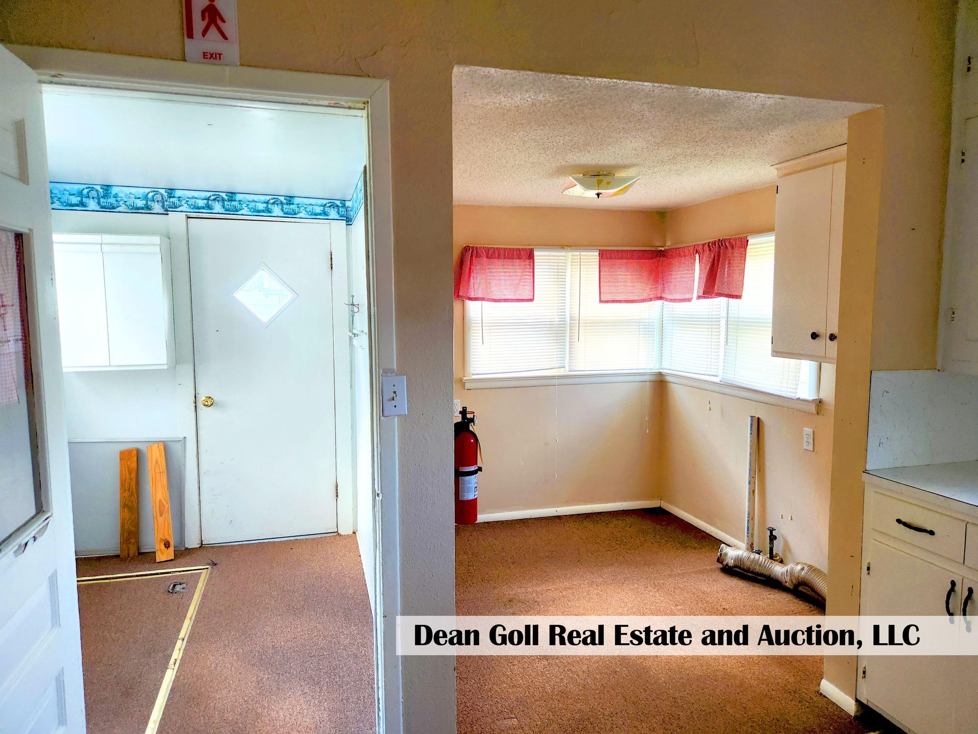 Interior view of a home: doorway leading to a small dining area with a window, red curtains, and white cabinets.