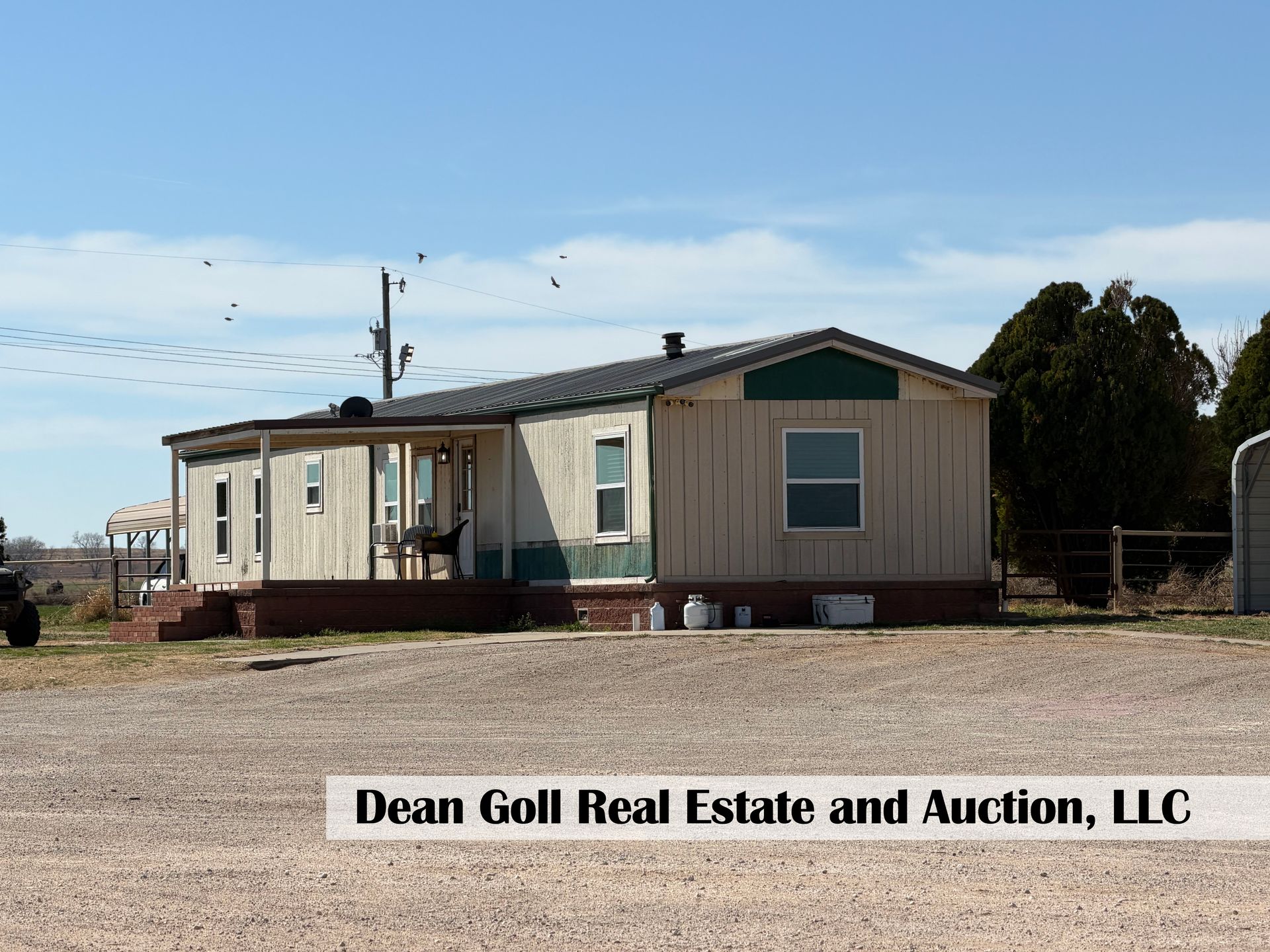 A single-story manufactured home with a porch, set on a gravel lot under a clear blue sky.