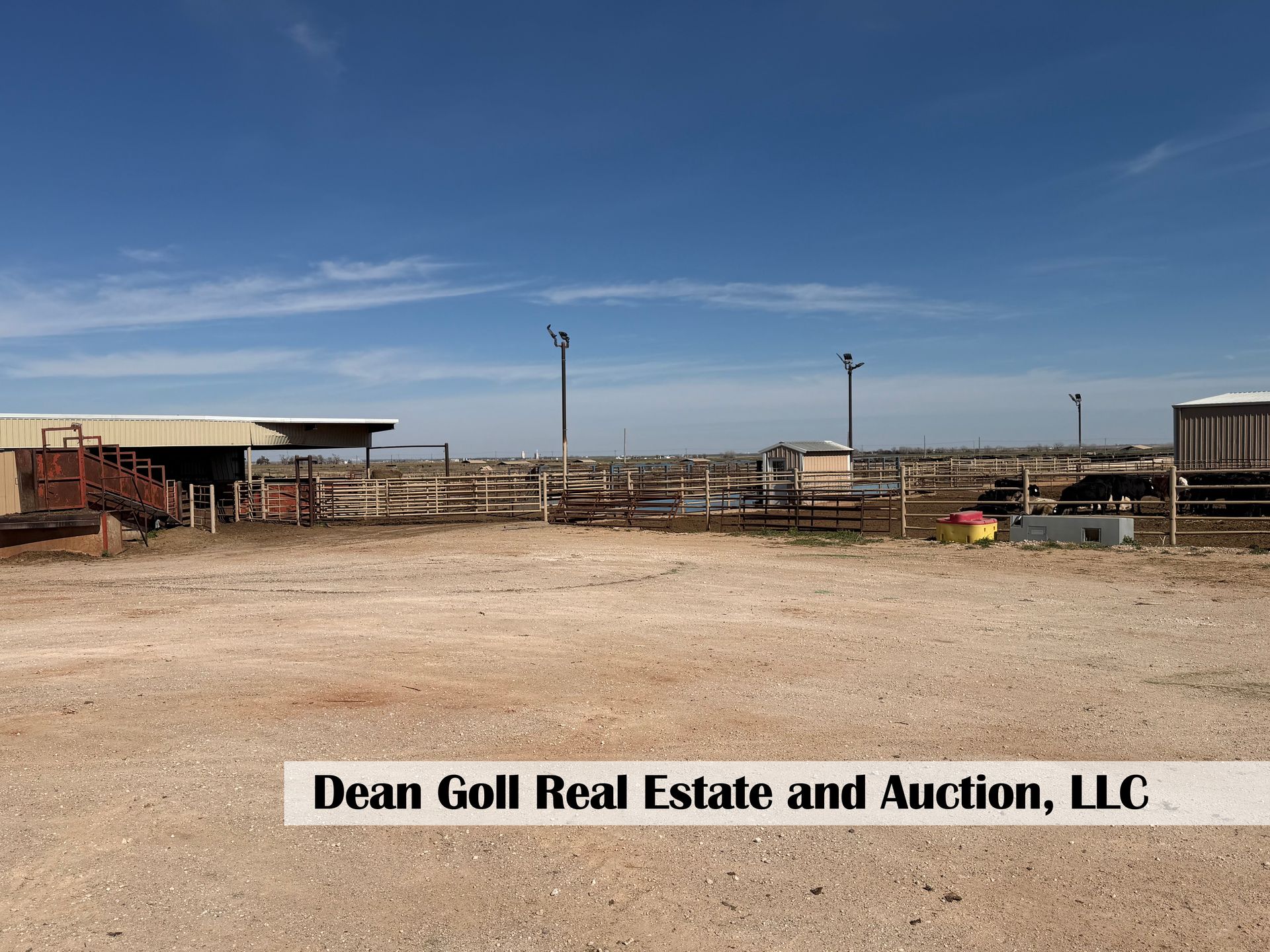 An open dirt lot with a cattle pen, shed, and light poles under a clear blue sky, branded for Dean Goll Real Estate.