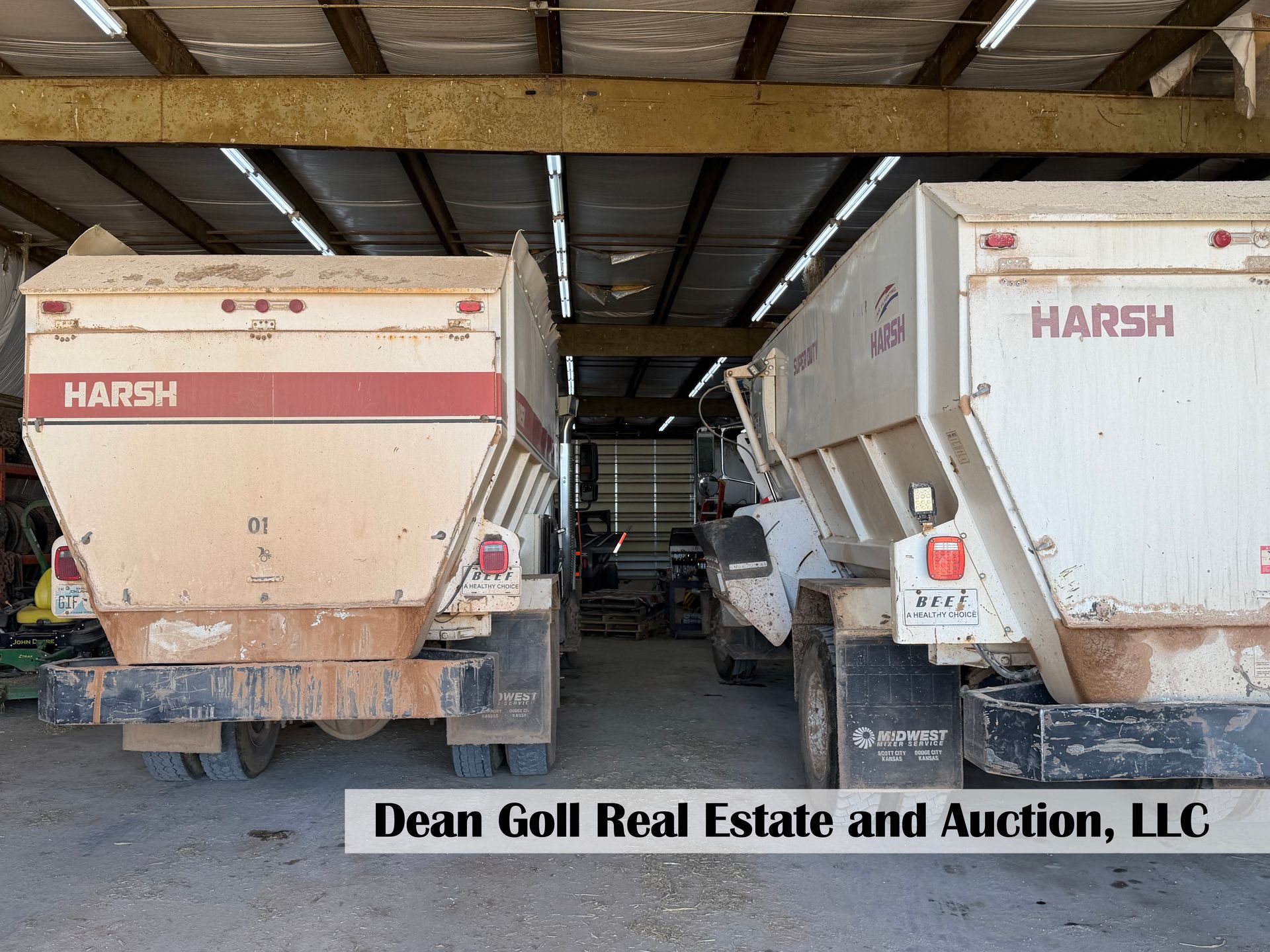 Two large white Harsh feed trucks parked side-by-side inside a barn at Dean Gull Real Estate and Auction.