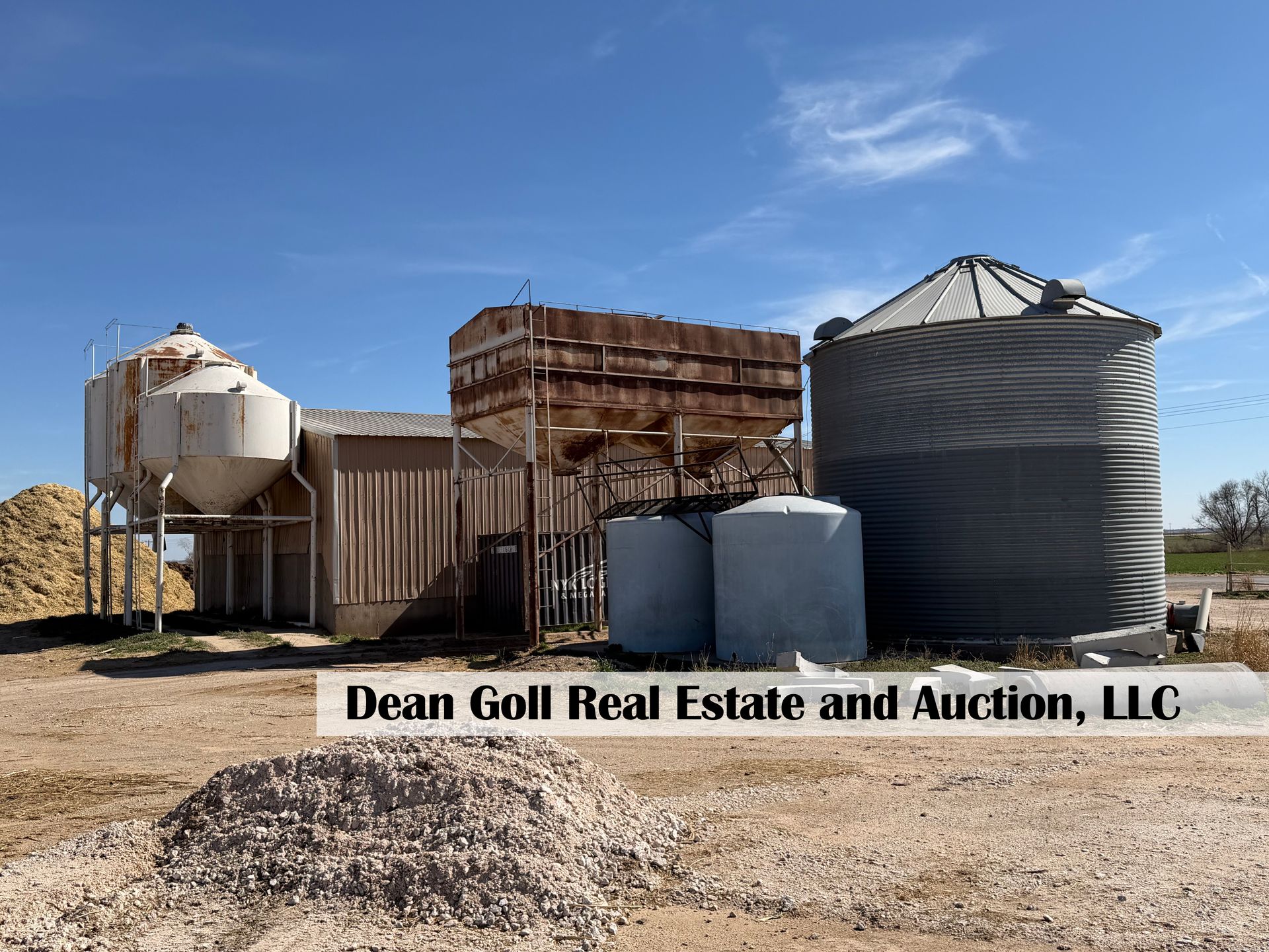 Farm structures, including metal grain silos and storage tanks, stand under a blue sky, with a branded text overlay.