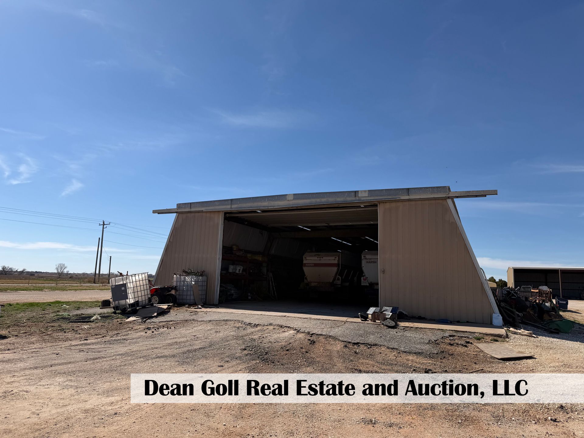 A wide, open-front metal shed on a dirt lot under a bright blue sky, with a branded text overlay at the bottom.