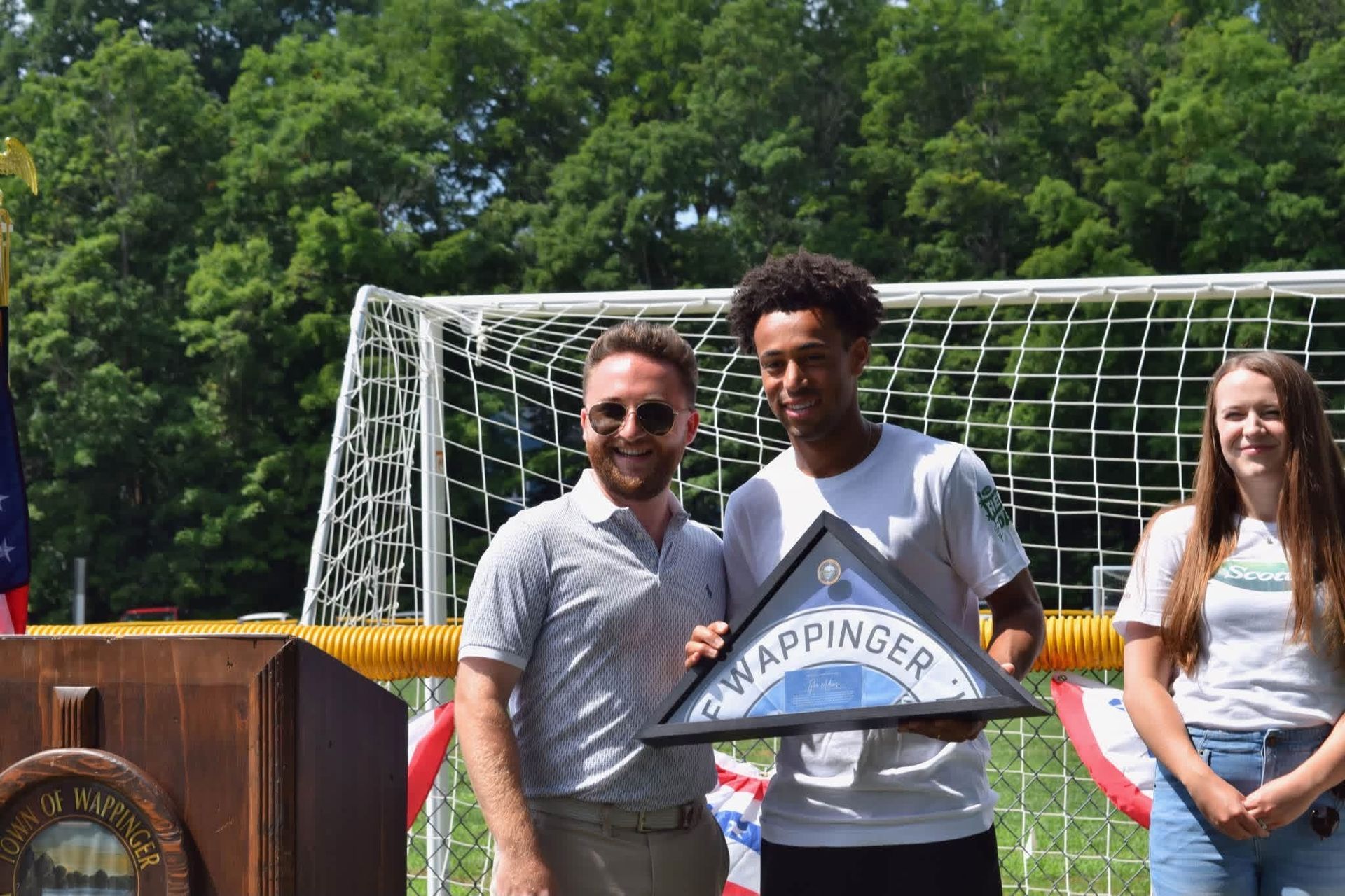 Two people holding a ribbon in front of a soccer goal at an outdoor event