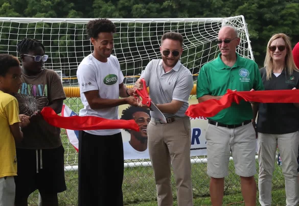 People cutting a red ribbon on a soccer field in front of a goal.