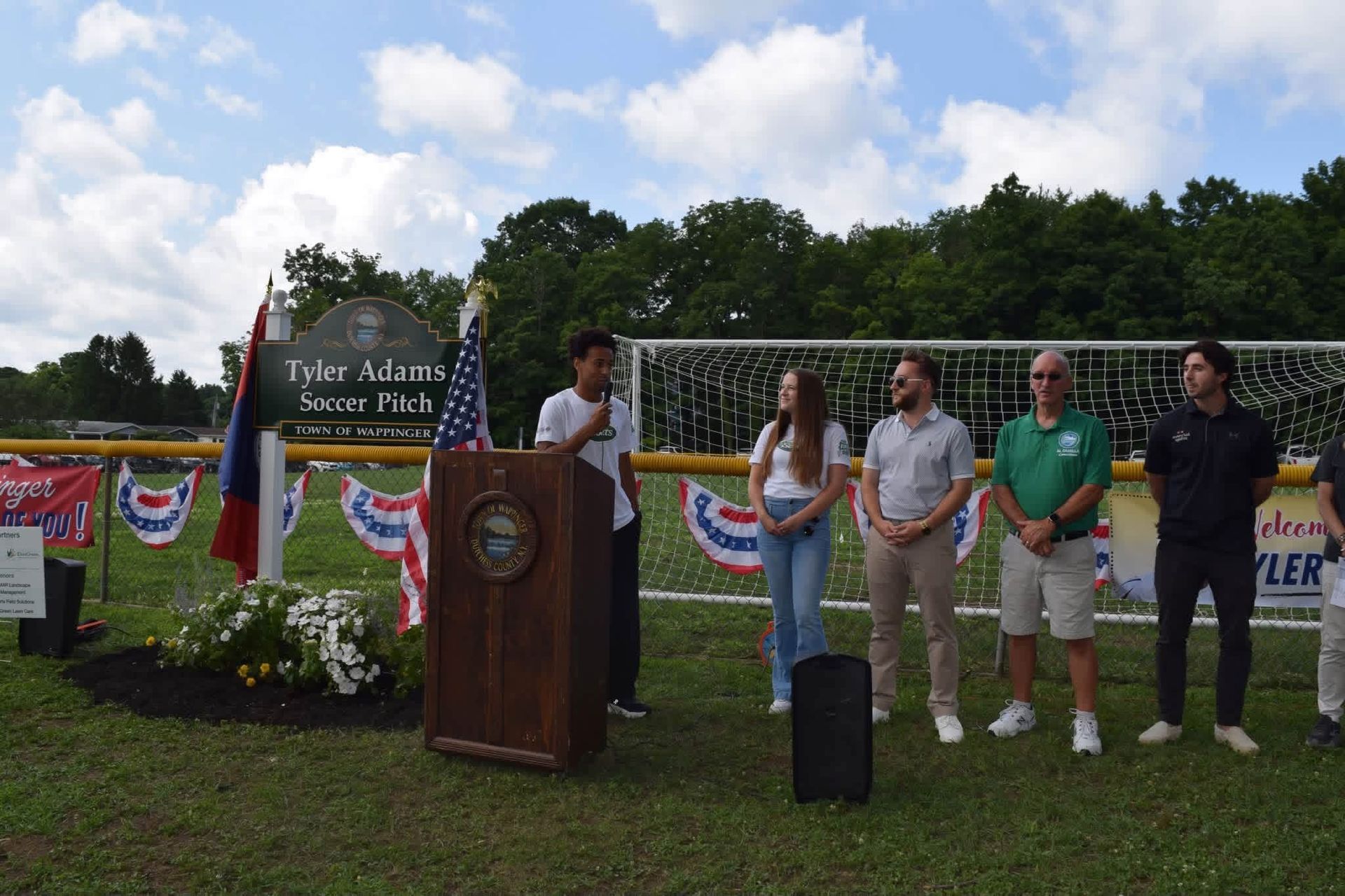 Outdoor ceremony with speakers at a podium in front of a “Twin Towers Star Park” sign and patriotic bunting.
