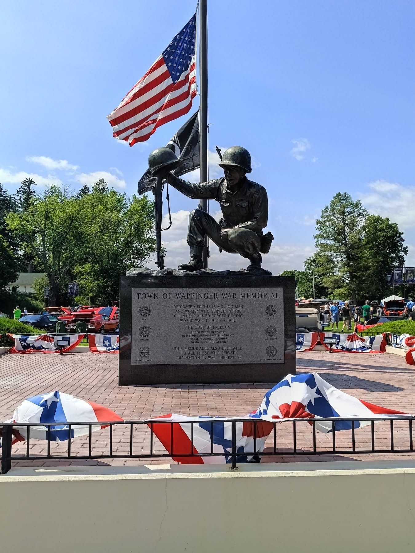 War memorial statue with U.S. flag, flowers, and red-white-blue bunting in a park